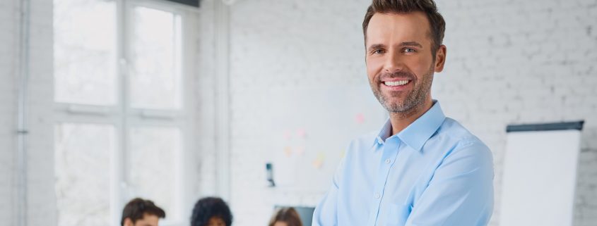Happy businessman standing in the office with coworkers in the b